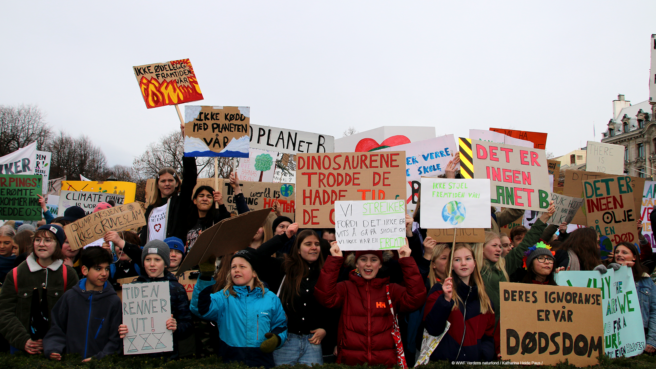 En stor gruppe ungdommer holder plakater med budskap om klimapolitikk.