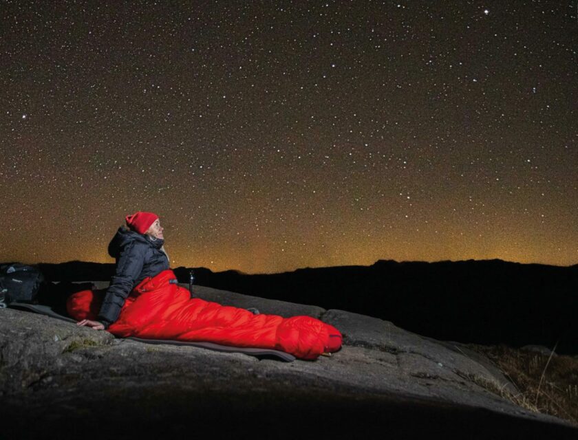 Dame med rød lue og rød sovepose ser opp mot en stjernekledd himmel