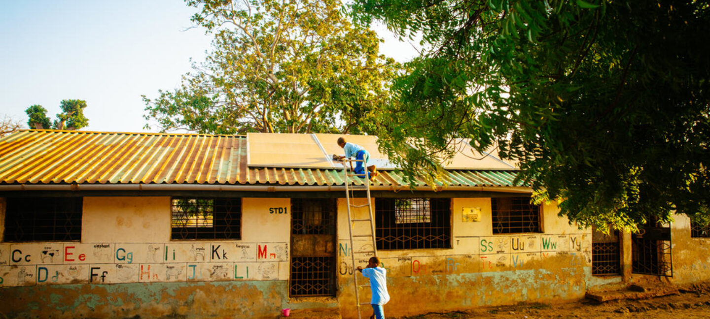 En gutt bruker stige til å klatre opp for å rengjøre solcellepanelet på skolens tak.
