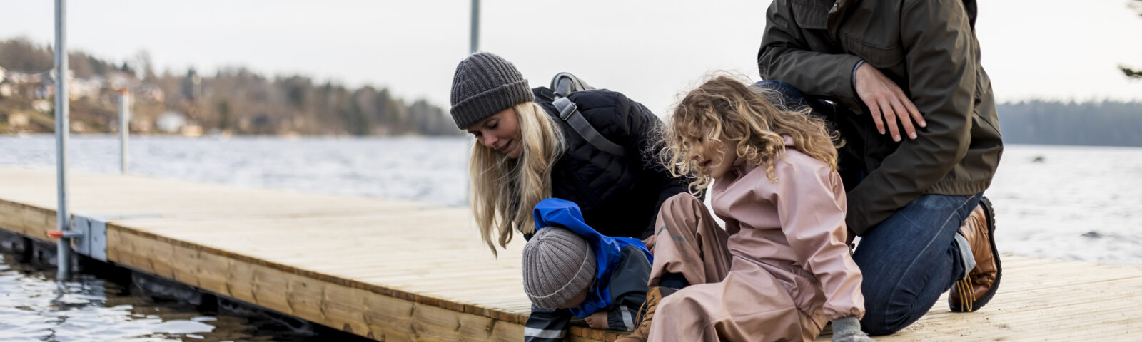 Familie sitter på brygga og kikker ned i vannet.