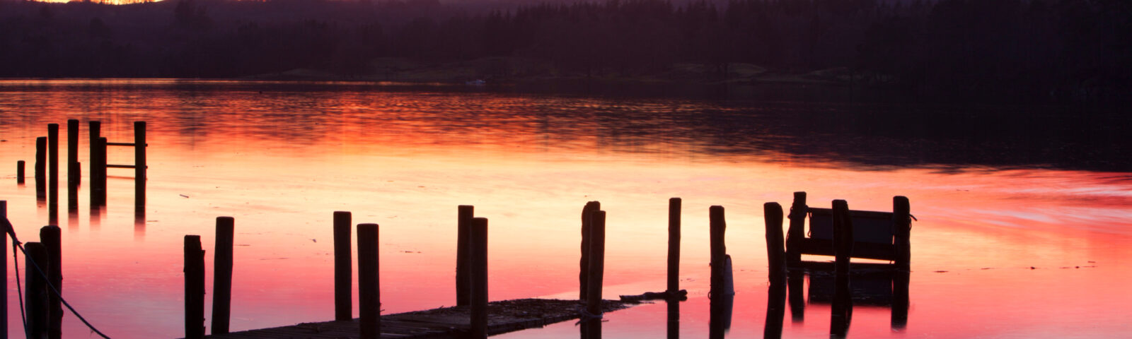 Den rødglødende solnedgangen speiler seg i en blikkstille innsjø.