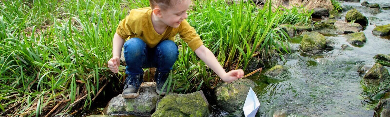 Gutt i elv med papirbåt