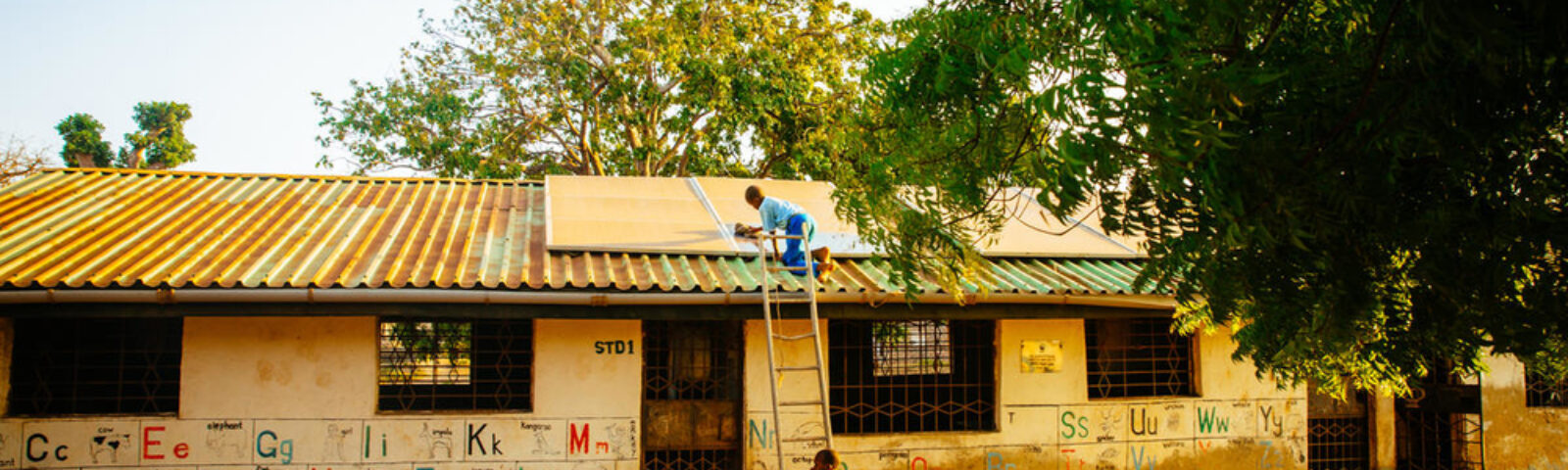 En gutt bruker stige til å klatre opp for å rengjøre solcellepanelet på skolens tak.