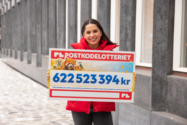 Jorun Stiansen fra Postkodelotteriet smiler og holder en sjekk på 622 523 394 kroner