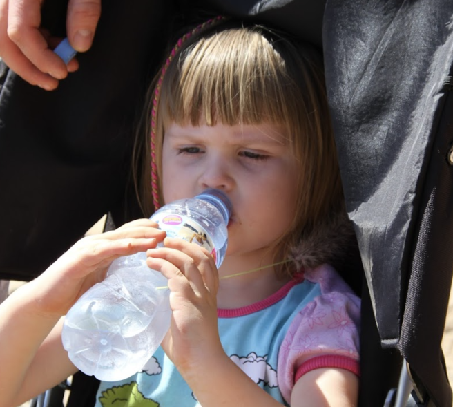 Liten jenten som drikker av en plastflaske.